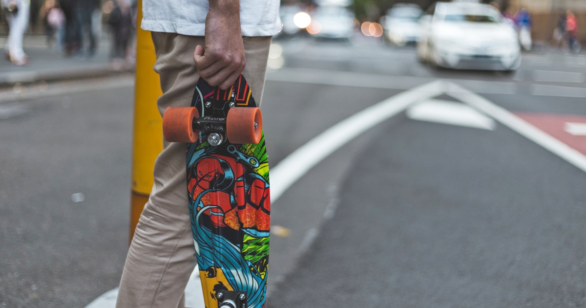 man holding a penny board in the street