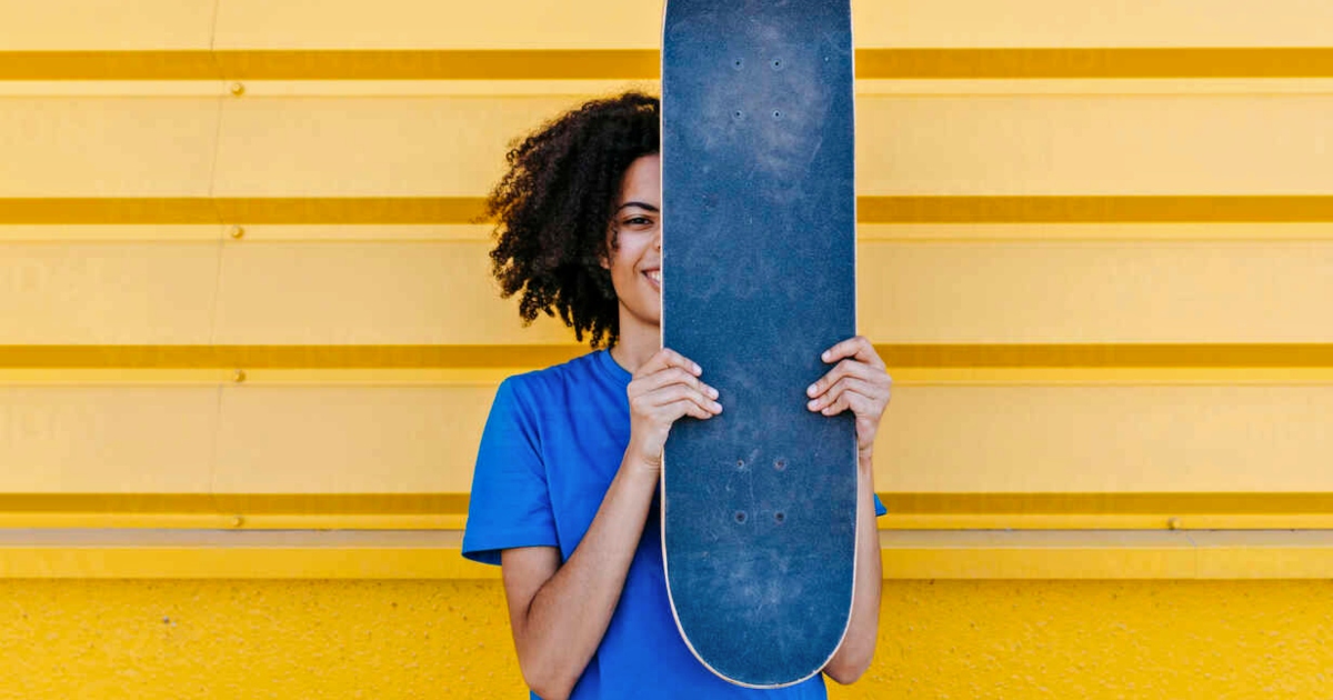 Portrait of African American woman with skateboard and yellow urban wall background in Granada, Spain. Woman urban wall african american afro yellow city blue